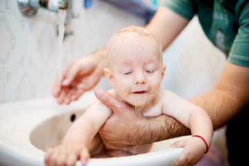 Happy laughing baby taking a bath. Little child in a bathtub. Smiling kid in bathroom. Infant washing and bathing. Hygiene and care for young children.