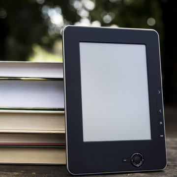 E-book and paper books on a wooden table in the courtyard amid the greenery