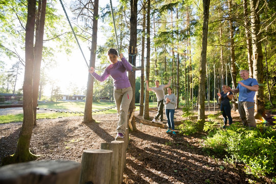 Friends Motivating Woman Crossing Log Bridge In Forest