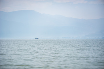 Small boat on a lake in the haze with mountains in the background, Xichang, China