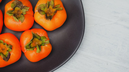 Ripe persimmon fruit on black plate and rustic white color table, tropical fruit