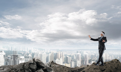 Young businessman in blindfold walking carefully and cityscape at background