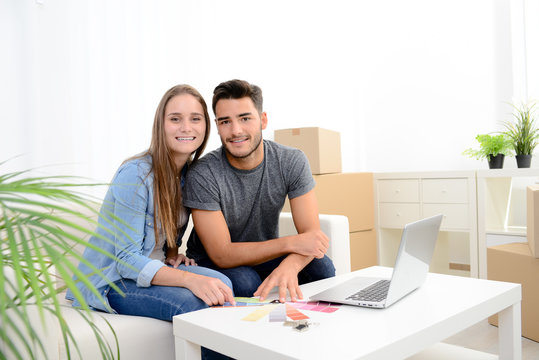 happy young couple student roommate making future project with internet computer at home while packing boxes and moving furnitures during move into their new home flat apartment