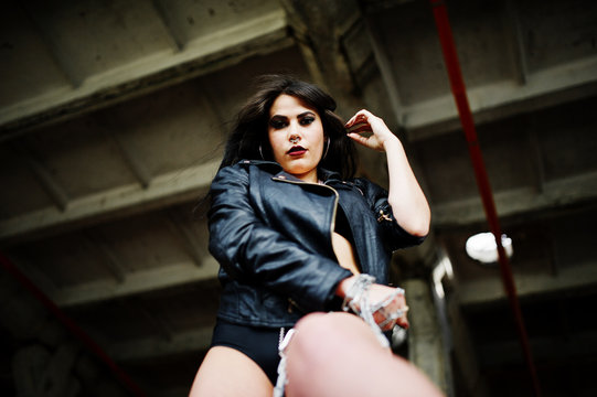 Brunette plus size sexy woman, wear at black leather jacket, lace panties, bra with chain at hands on abadoned place. BDSM theme.
