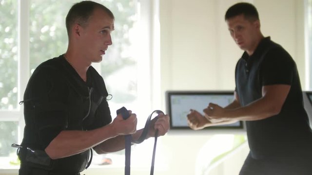 EMS training - muscular fitness instructor works with athlete wearing ems suit - working for arms