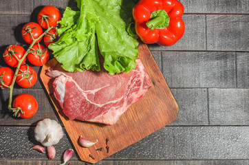 A raw piece of beef with peppers, tomatoes, herbs and garlic