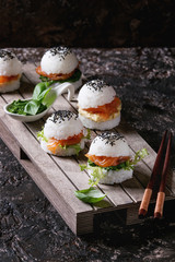 Mini rice sushi burgers with smoked salmon, green salad and sauces, black sesame served on wood...