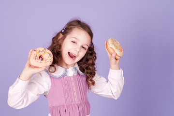 Laughing baby girl 4-5 year old eating donuts. Looking at camera. Childhood. Unhealthy lifestyle.