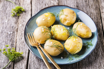 Young boiled potatoes with dill and olive oil, sprinkled a sea salt on a plate on rustic wooden...