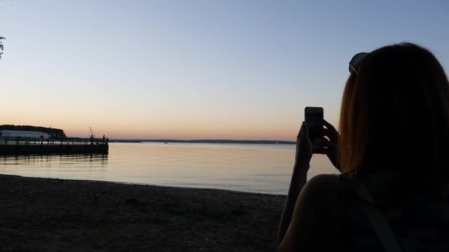 Girl shoots on a smartphone video about the sunset on the sea.