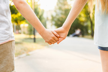 young boy and girl hold hands and stroll in the park in sunny weather