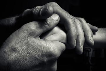 Hands of an elderly man holding the hand of a younger man.