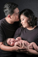 family portrait of young asian mum and dad and boy newborn in black background .