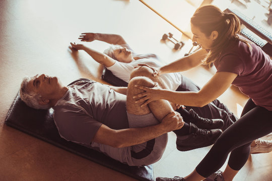Senior couple workout in rehabilitation center. Personal trainer helps elderly couple to do stretching on the floor.