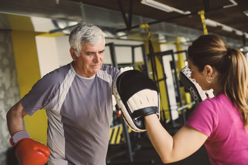 Fototapeta na wymiar Older man boxing in gym. Senior man with personal trainer.