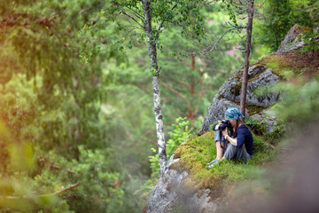 Beautiful girl tourist stands on a rock to photograph nature with a digital camera in the jungle on a high mountain. Holiday Travel Concept.