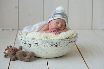 The newborn boy lies in a round bowl on a white plaid and sleeps sweetly with his hands under his head