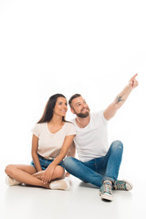 'portrait of young attractive couple sitting on floor looking somewhere, isolated on white