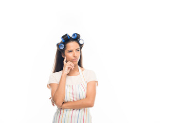 'Young thoughtful housewife with curlers, wearing apron, isolated on white