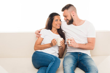 'portrait of young attractive couple having coffee sitting on couch, isolated on white