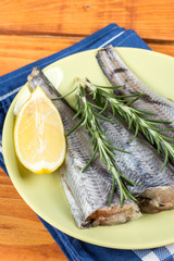 Above green plate with fresh hake fish and rosemary and lemon