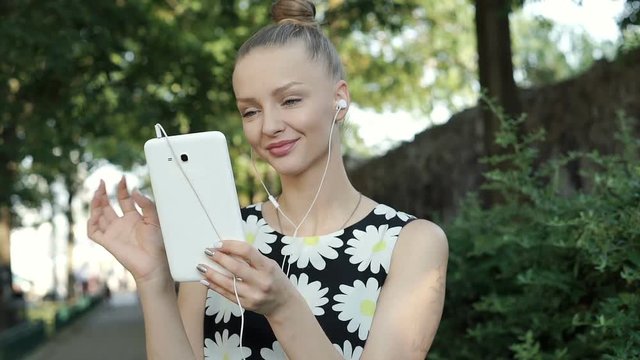 Pretty girl in floral shirt listening music and browsing internet on tablet, steadycam shot
