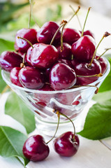 Ripe maroon cherries in a glass vase and a jar