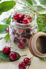 Ripe maroon cherries in a glass vase and a jar