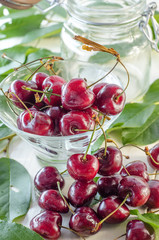 Ripe maroon cherries in a glass vase and a jar