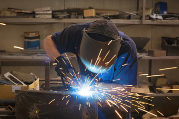 Male in face mask welds with argon-arc welding