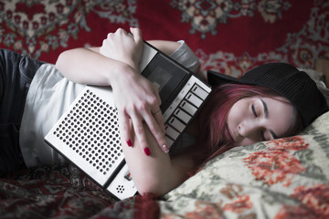 A girl is sleeping with an old cassette tape recorder in her hands