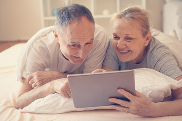 Senior couple enjoying at home and watching something on the tablet before sleeping.