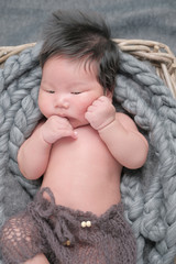 cute asian boy newborn portrait  with white doll one month lie down  on grey background fabric in basket with hands of his dad .