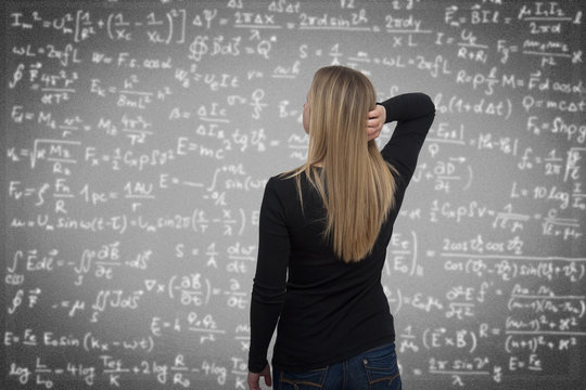 Frau steht vor einer Tafel mit vielen Formeln