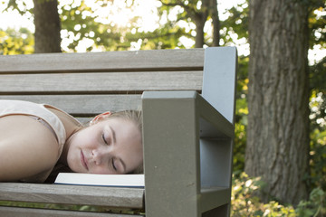 Junge Frau liegt auf Parkbank und ist auf Buch eingeschlafen