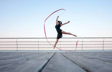 Fototapeta premium Young beautiful ballerina doing gymnastic jumps outdoors near the sea