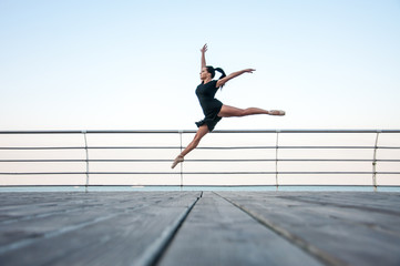 Fototapeta na wymiar Young beautiful gymnast doing gymnastic jumps outdoors near the sea