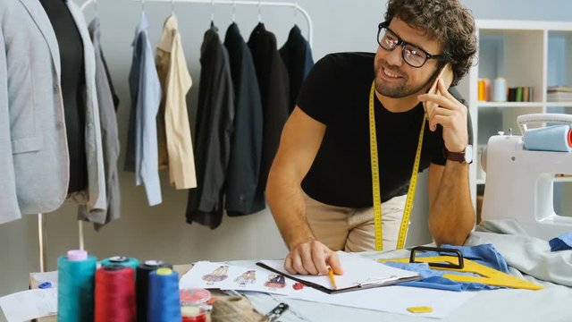 Young fashion designer talking on smart phone with customer and writing down the new big order.
