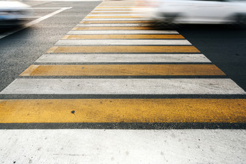 Road marking. Yellow and white stripes on the asphalt surface in the city, against the background of passing cars.