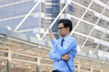 Portrait of handsome young Asian businessman with formal clothes holding mobile smart phone at outside office background.