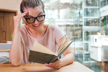 Relaxed smiling girl reading book in cafe at shopping mall