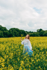 Fototapeta premium Beautiful girl in a dress among yellow flowers in a field