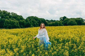 Fototapeta premium Beautiful girl in a dress among yellow flowers in a field