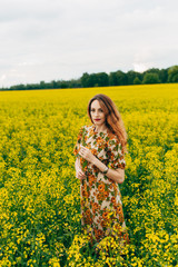 Naklejka na ściany i meble Beautiful girl in a dress among yellow flowers in a field