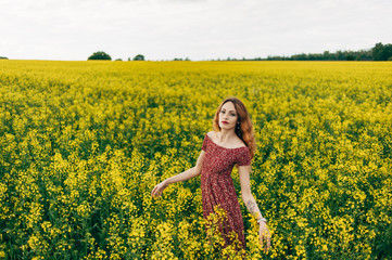 Fototapeta premium Beautiful girl in a dress among yellow flowers in a field