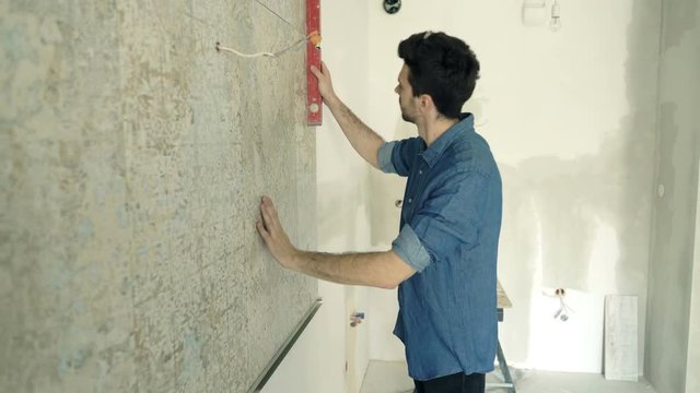 Young man checking wall with level at new home 
