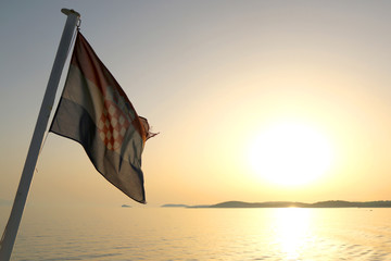 Croatian flag on a boat, blowing in the wind. Beautiful coast in the background. Selective focus.
