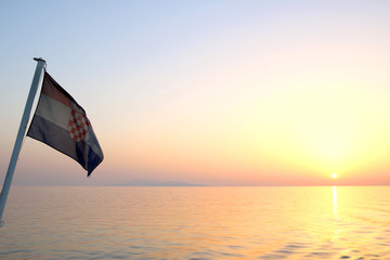 Croatian flag on a boat, blowing in the wind. Beautiful coast in the background. Selective focus.
