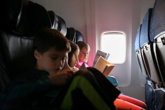 Three children reading books on airplane journey