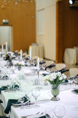 covered festive table for a wedding dinner in a white summer style with bouquets of tulips. In the bright banquet hall.